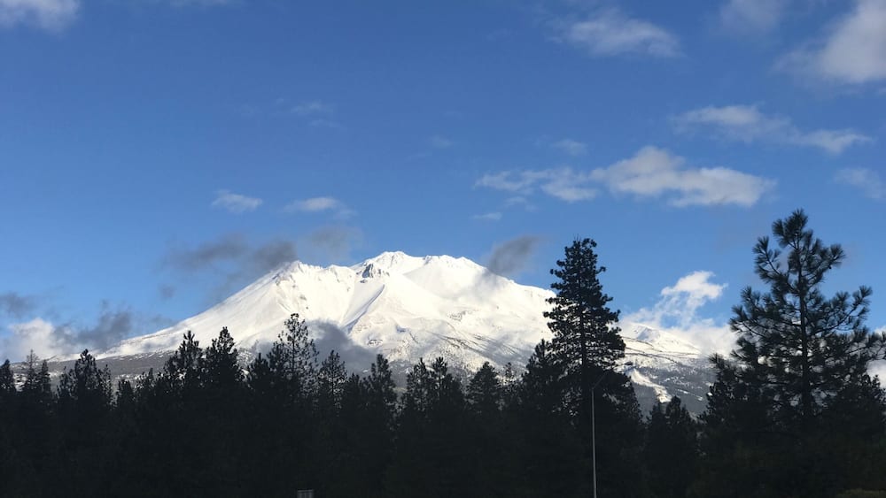 A snow-capped mountain with a clear blue sky and a road with a car in the foreground.