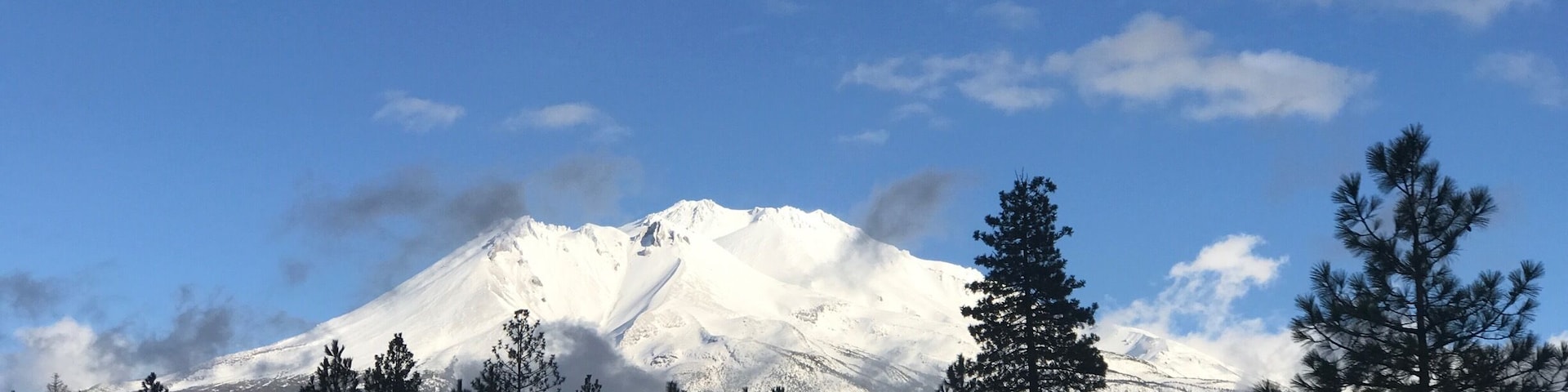 Montaña nevada bajo un cielo azul despejado, con un camino y un coche en primer plano.