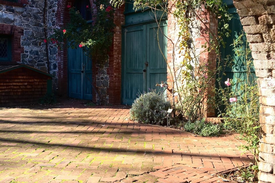 Un patio con un camino de ladrillo, un edificio de piedra con una puerta verde y una lámpara colgante.