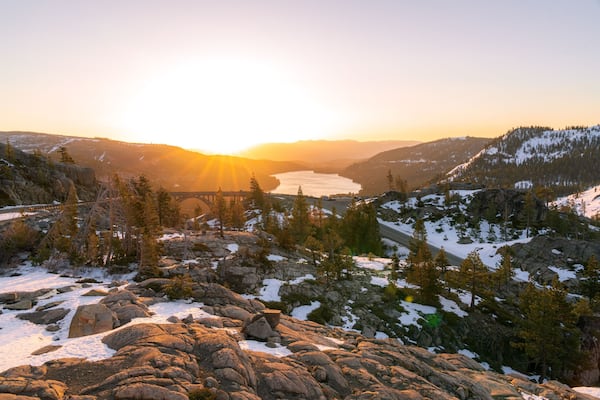 Paisagem montanhosa com rio, picos nevados e uma ponte.