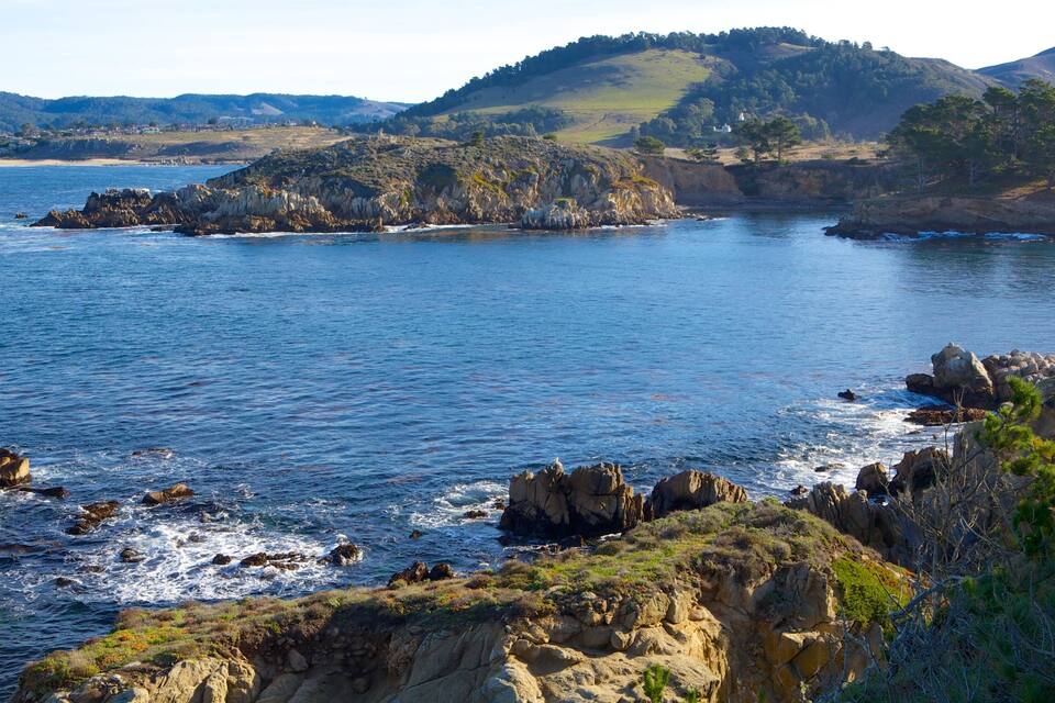 A coastal landscape with rocky shores, calm sea, and distant hills.