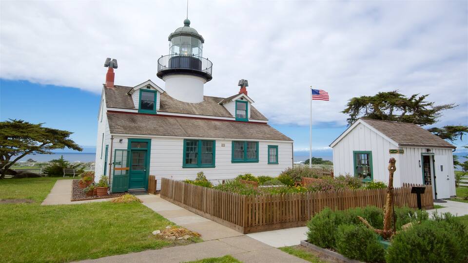 A white lighthouse with a green door and windows, a small white building with a green door, and an American flag.