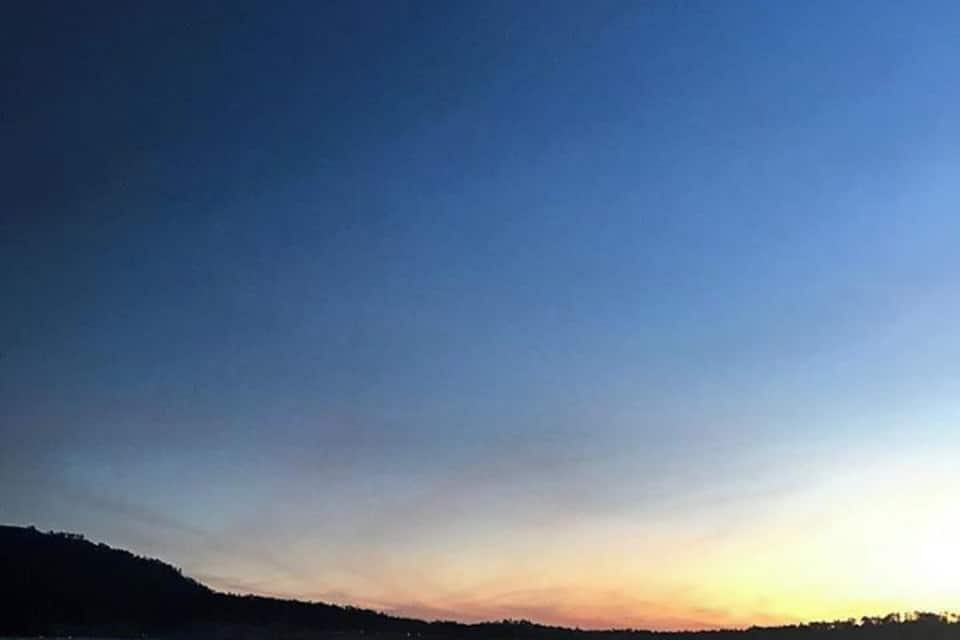 A beach at sunset with a calm sea and a crescent moon in the sky.