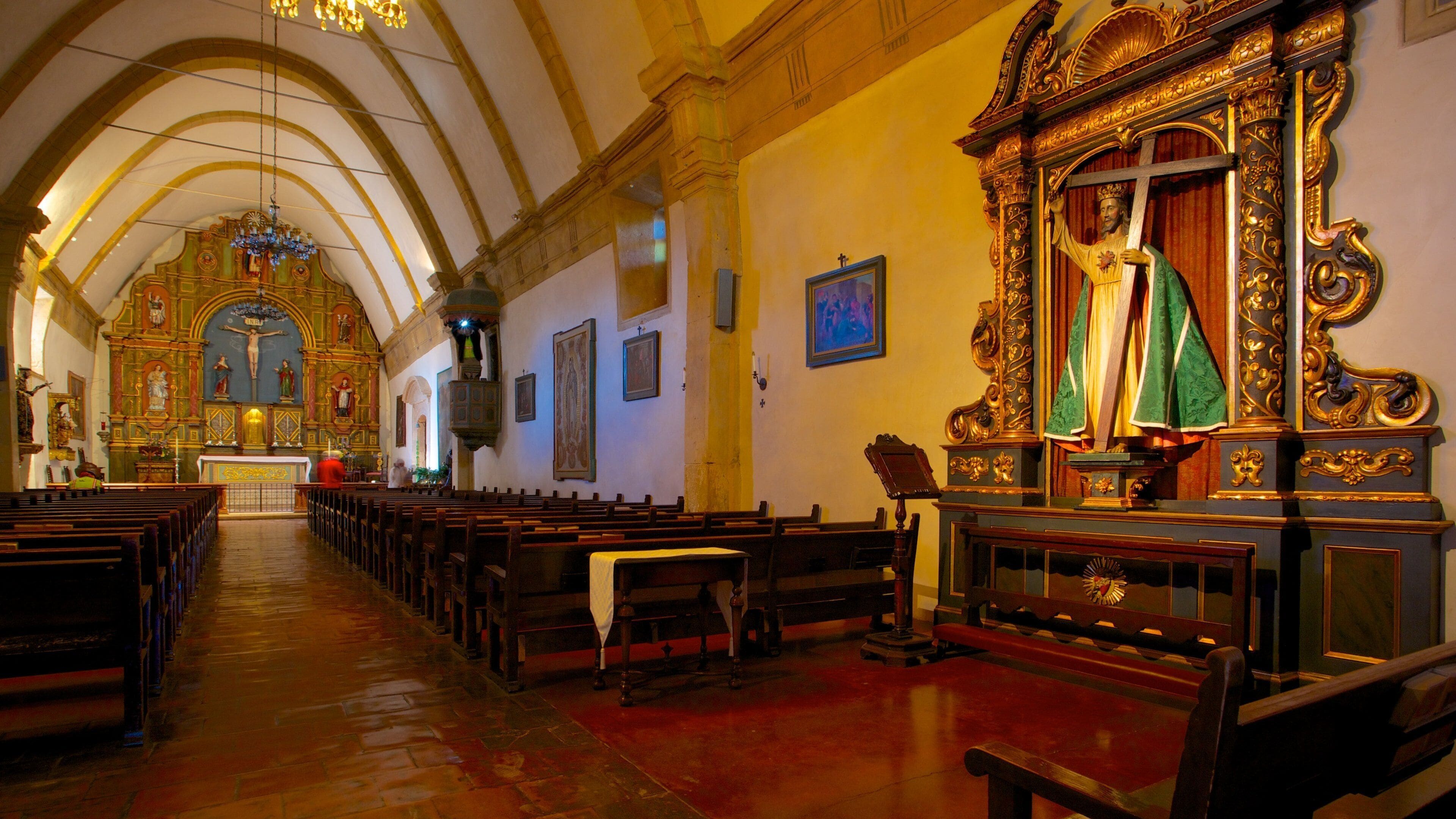 An ornate church interior with wooden pews, a crucifix, and a statue of Jesus.