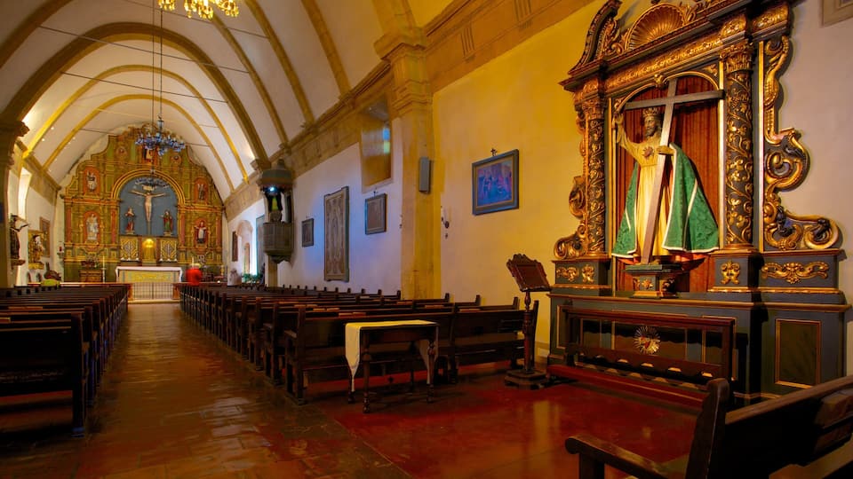 An ornate church interior with wooden pews, a crucifix, and a statue of Jesus.