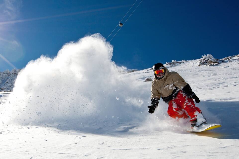 A snowboarder carving through snow with a large spray of snow behind them.