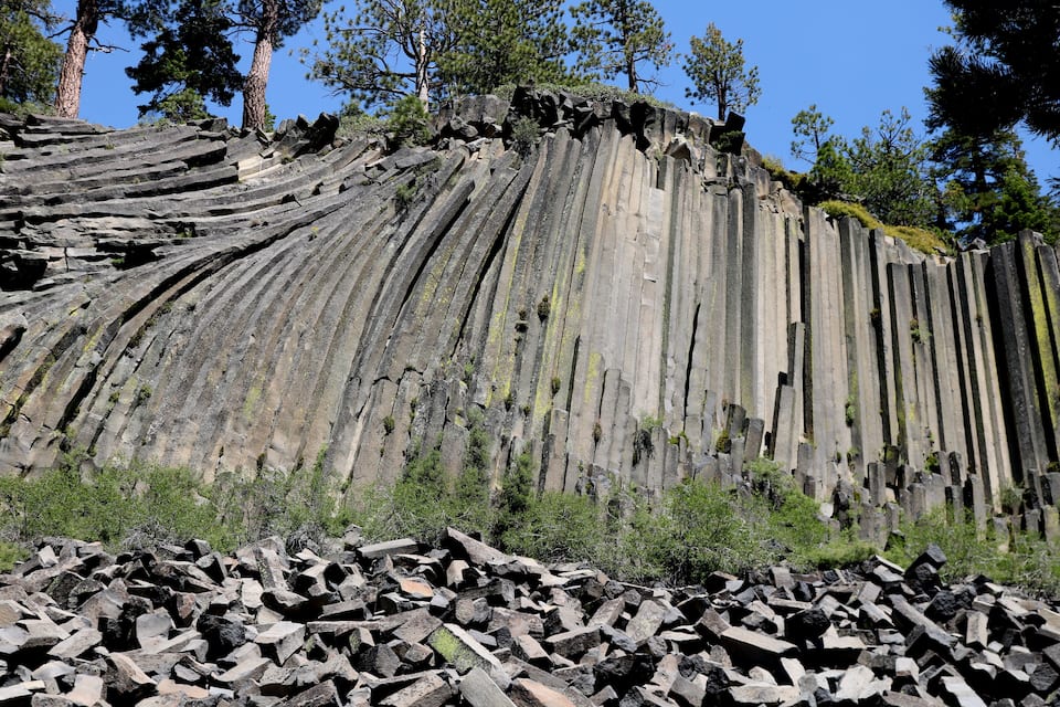 A large rock formation with vertical striations and a pile of broken rocks at its base.