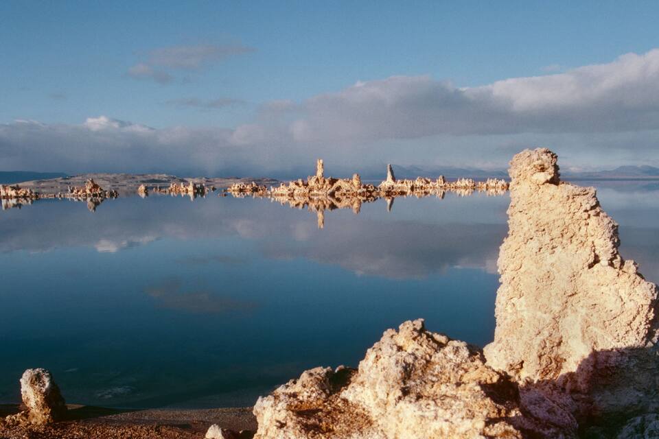 Un lago tranquilo con formaciones rocosas en primer plano y montañas al fondo.
