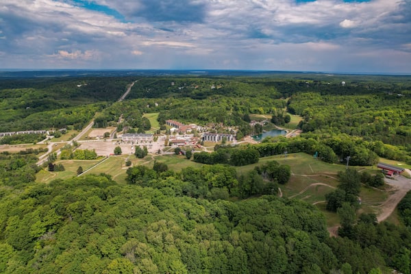 An aerial view of a park with a large building complex, a lake, and surrounding forested areas.