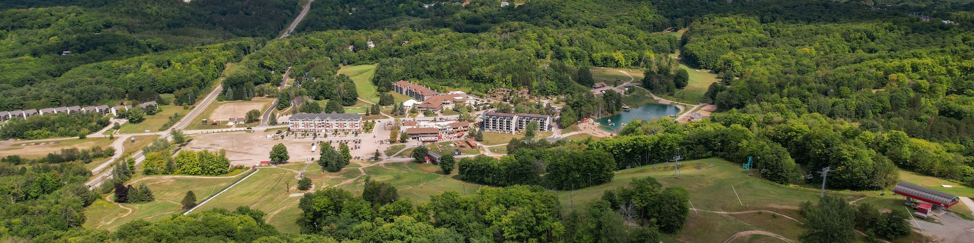 An aerial view of a park with a large building complex, a lake, and surrounding forested areas.