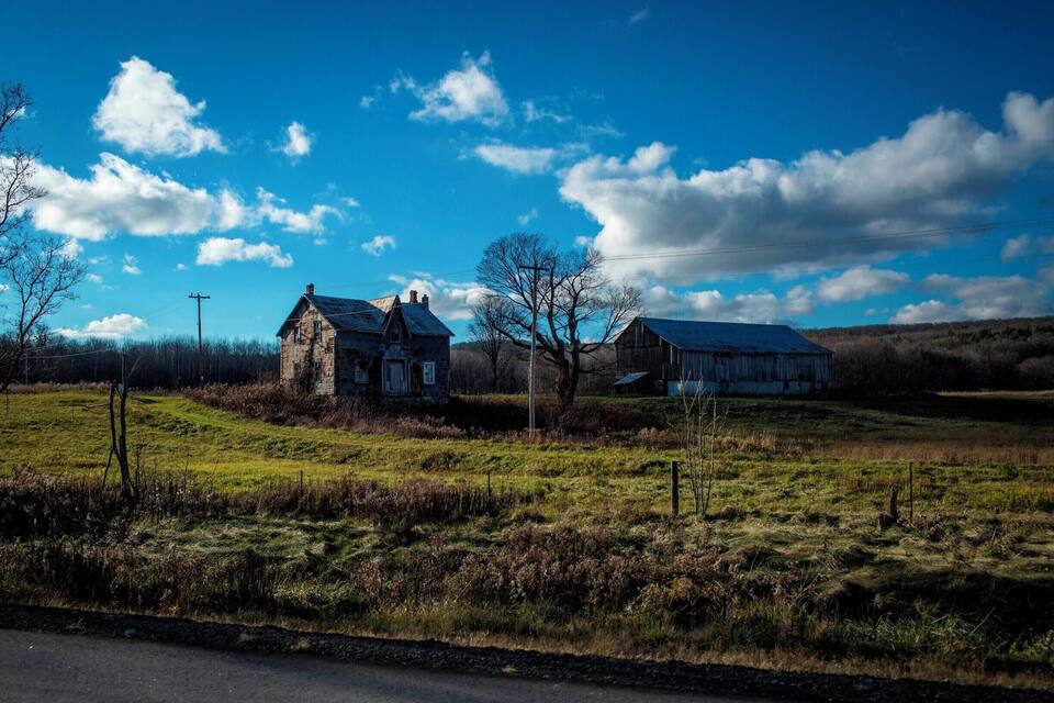 A rural landscape with a stone house and a barn.