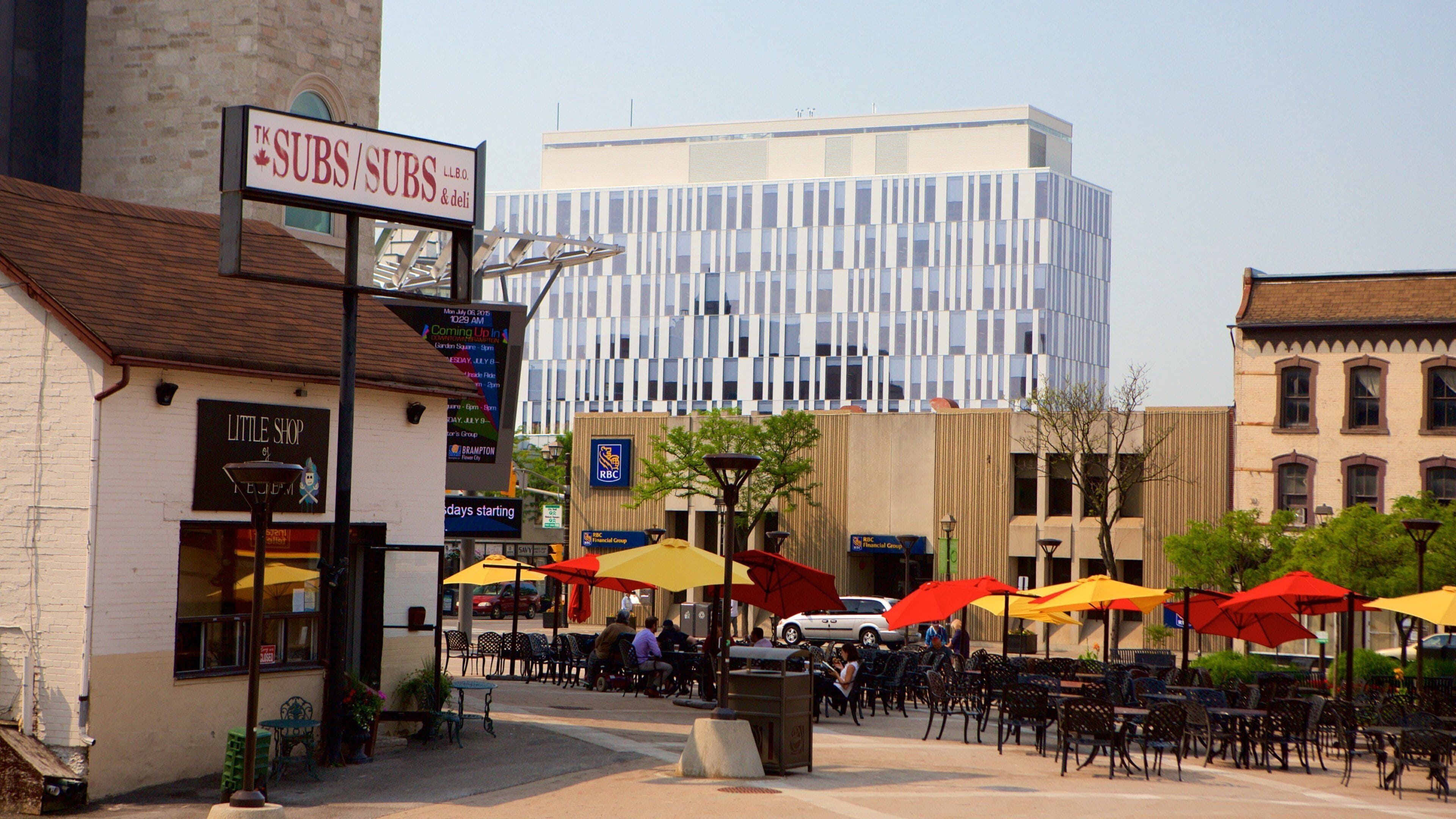 A downtown area with outdoor seating, a modern building, and a sign for 'TK SUBS & Deli'.