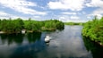 A river with a boat, surrounded by dense green forest and a clear sky.