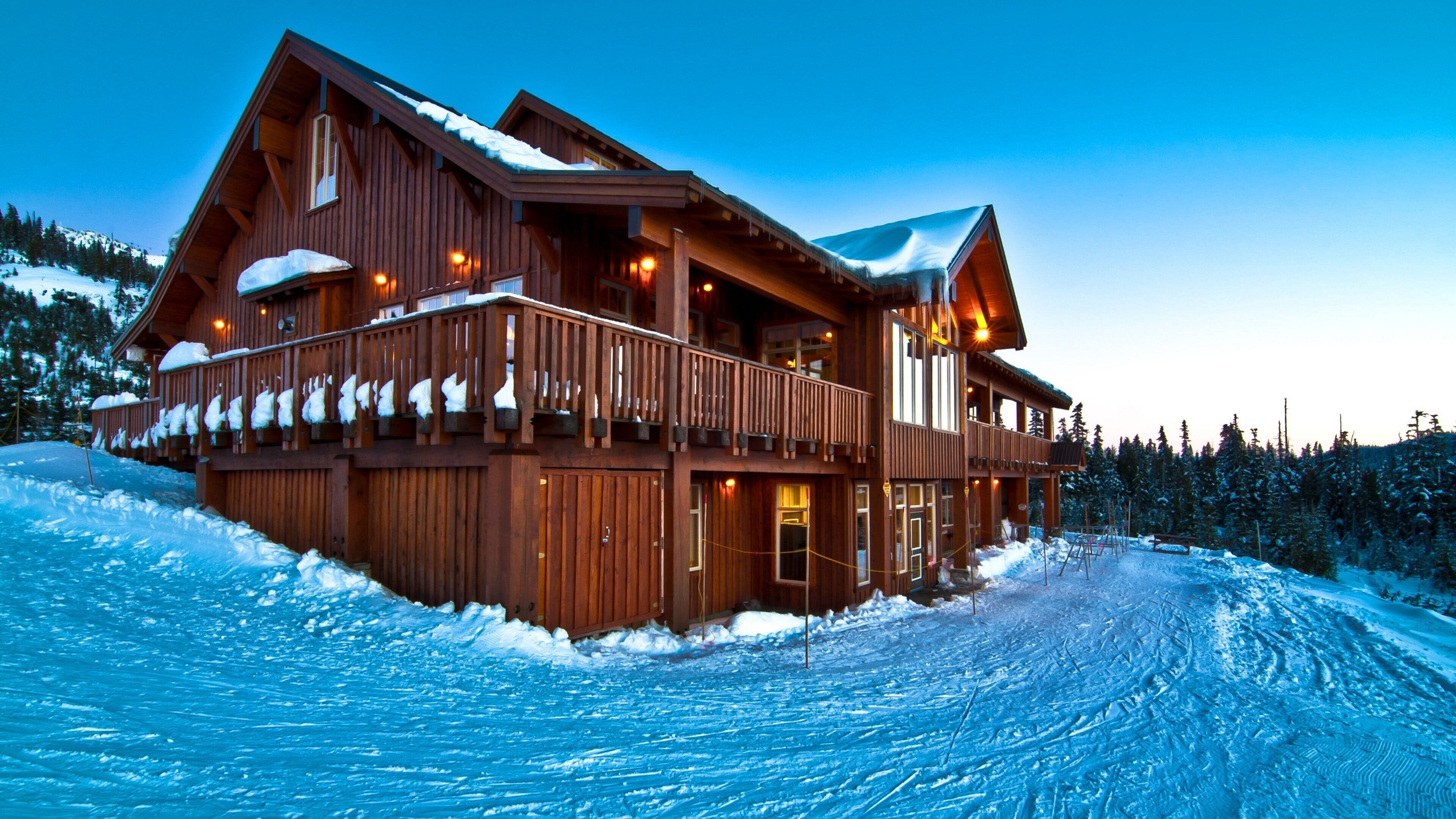 A wooden lodge with a balcony and snow-covered roof, surrounded by a snowy landscape.