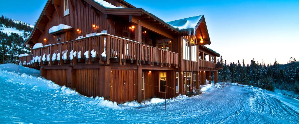 A wooden lodge with a balcony and snow-covered roof, surrounded by a snowy landscape.