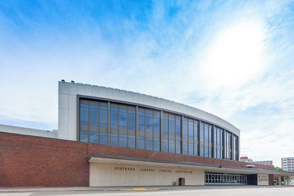En modern byggnad med stora fönster och ett välvt tak, med skylten "Northern Alberta Jubilee Auditorium".