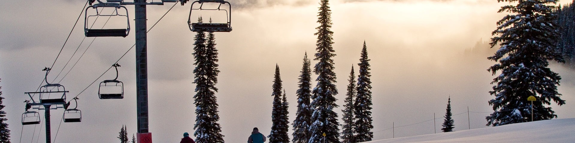 A ski lift, snow-covered trees, and a mountain range in the background.