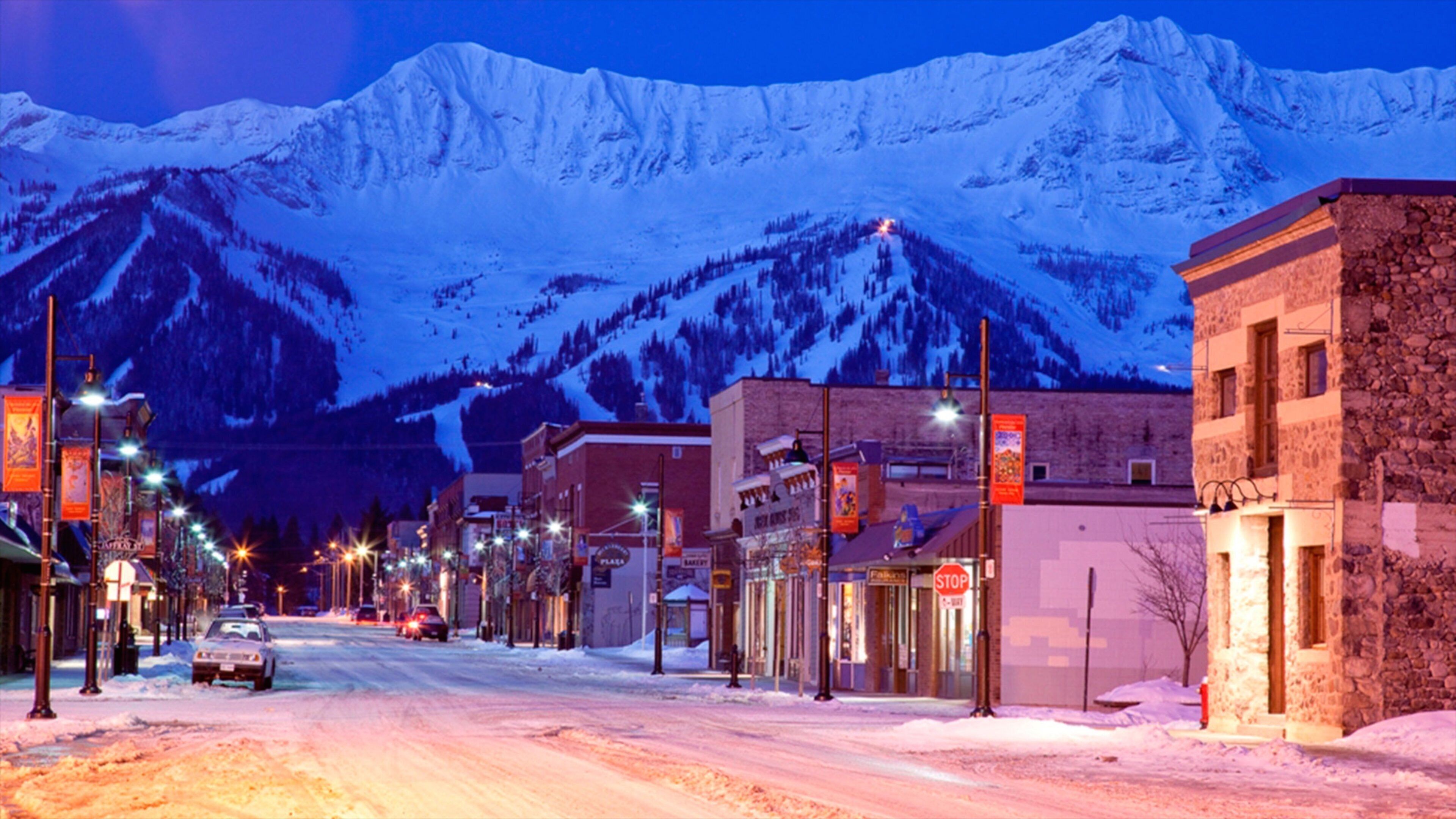 A snow-covered street with buildings and a mountain in the background.