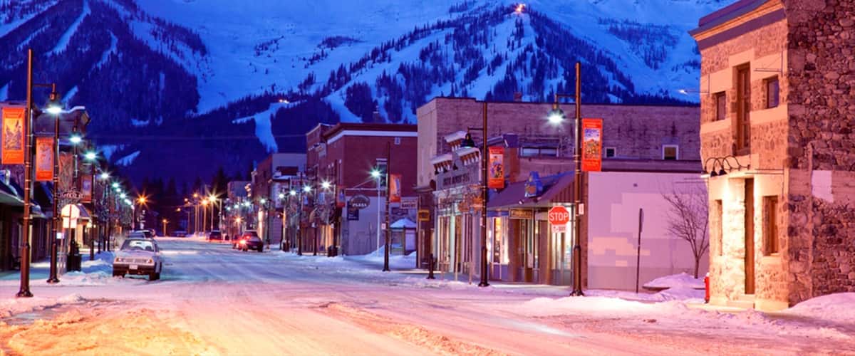 A snow-covered street with buildings and a mountain in the background.