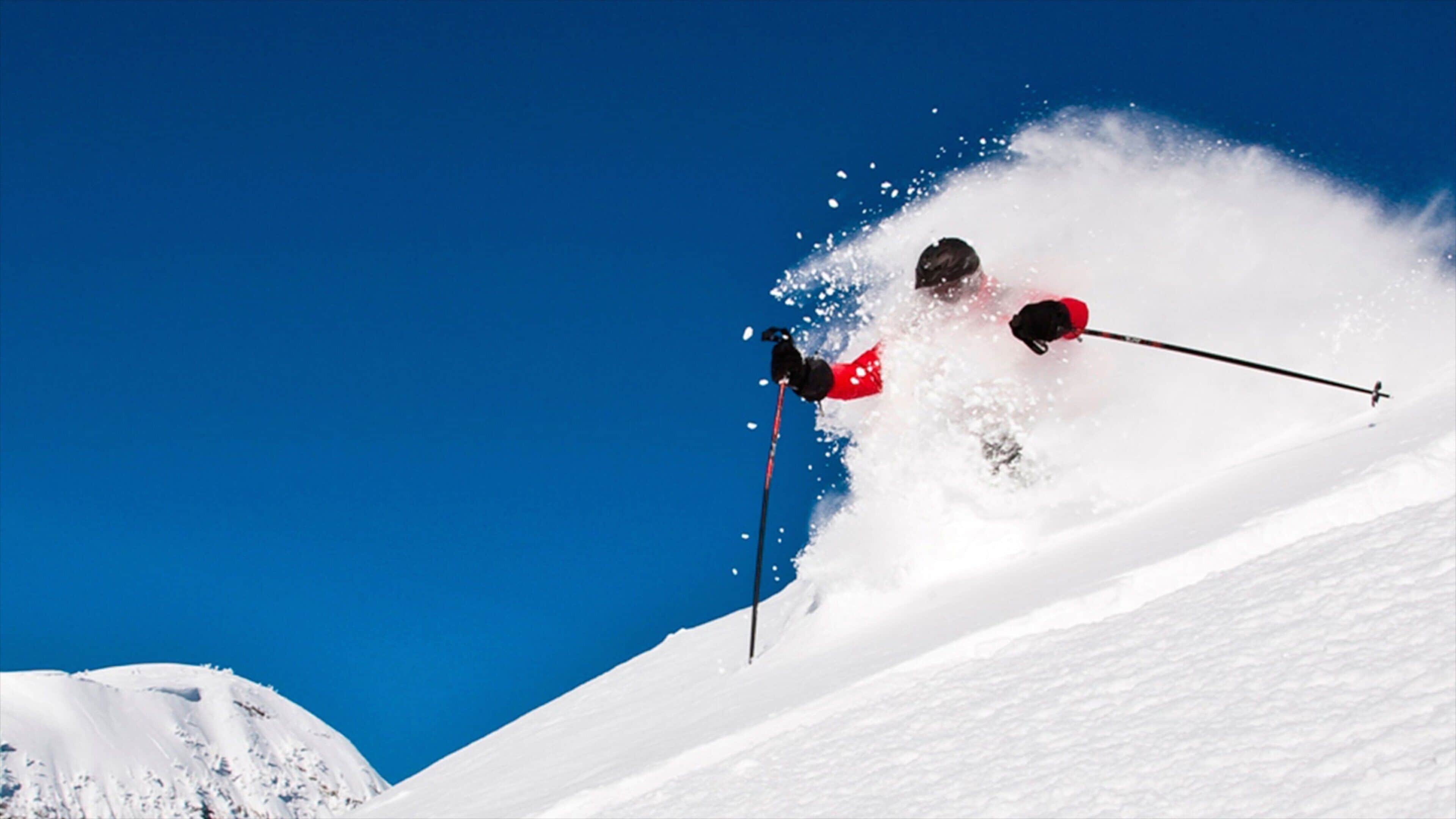 A skier in mid-air with a clear blue sky in the background.