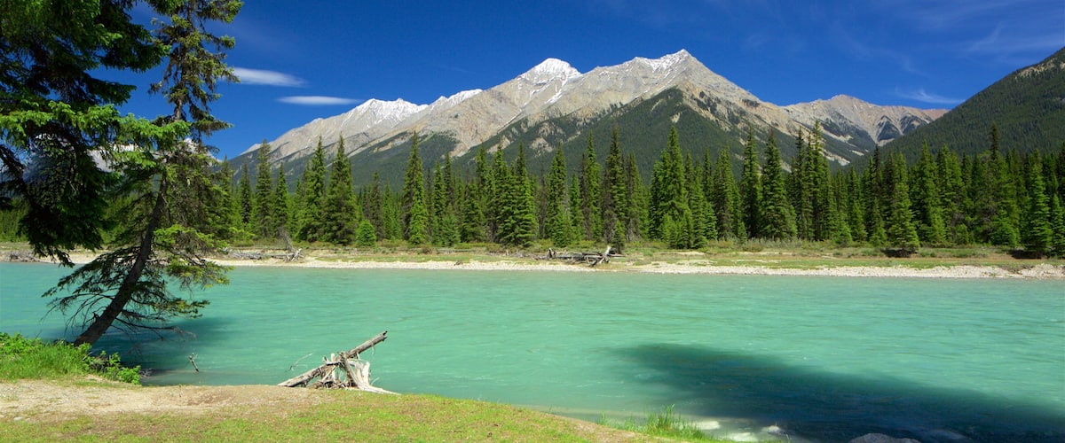 A mountain range with a clear blue sky, a turquoise river, and dense green forests.