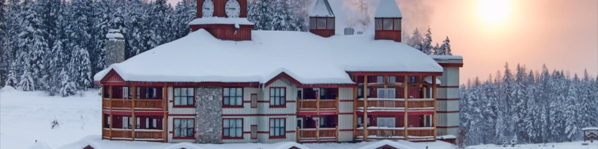 A large wooden lodge with multiple chimneys and a snow-covered roof, surrounded by a snowy landscape and dense trees.