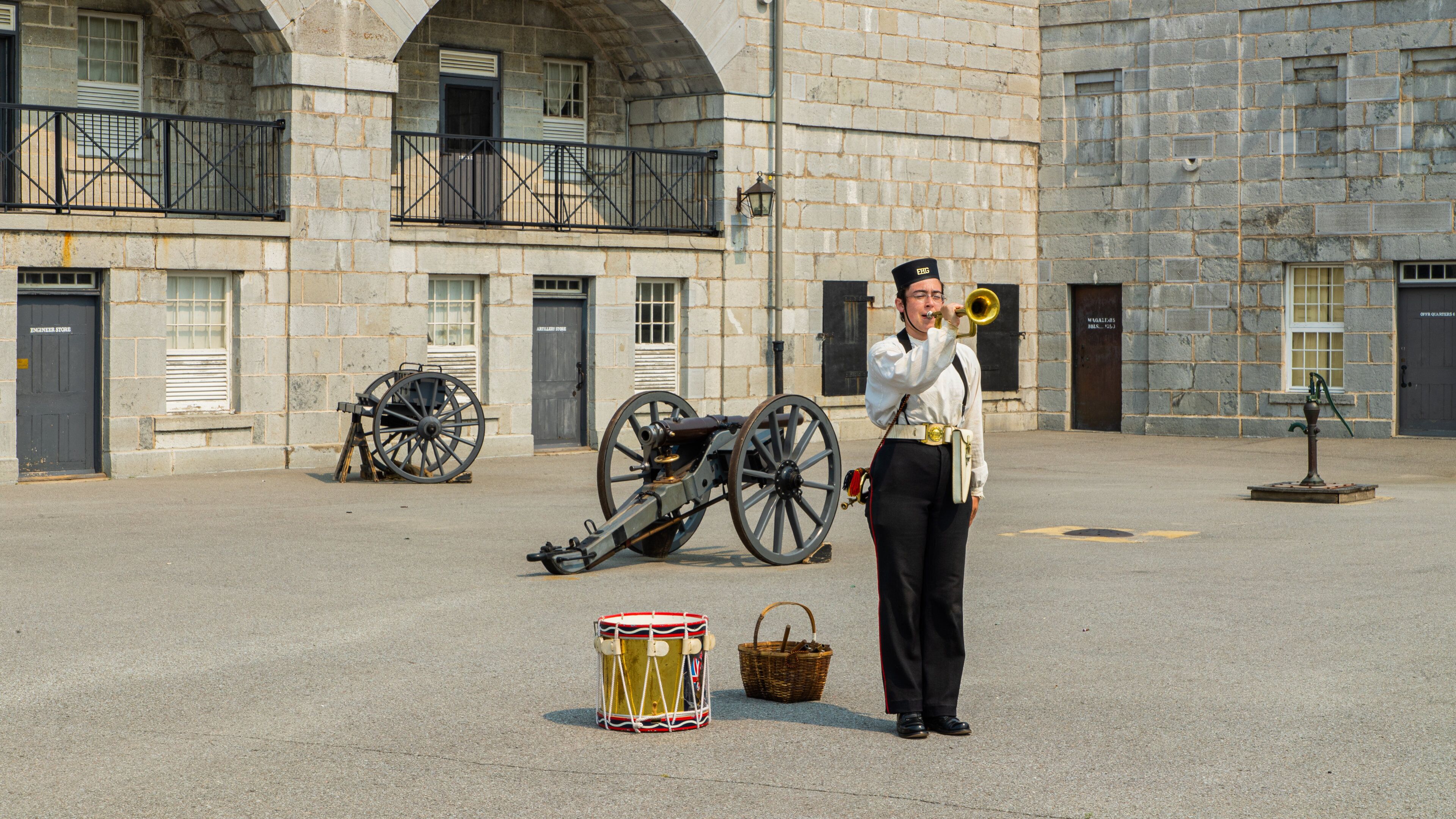 A historical building with stone architecture, a cannon, and a drummer in period attire.