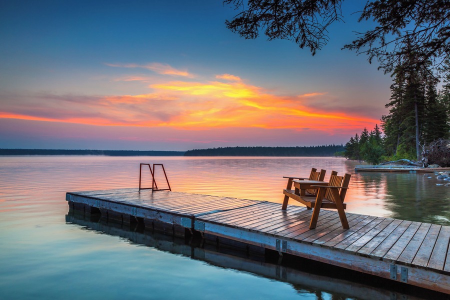 Bench sitting on the dock as a colourful sunrise lights up the sky over Clear Lake, in Riding Mountain National Park, Manitoba Canada