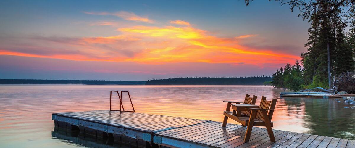A wooden dock extending into calm water with a sunset in the background.