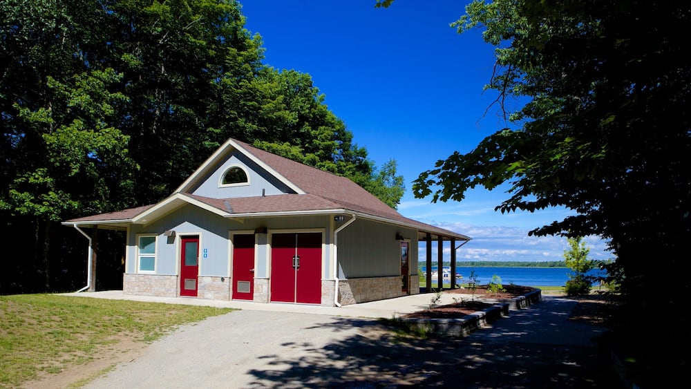 A small building with a red door and a covered porch, surrounded by trees and a lake.