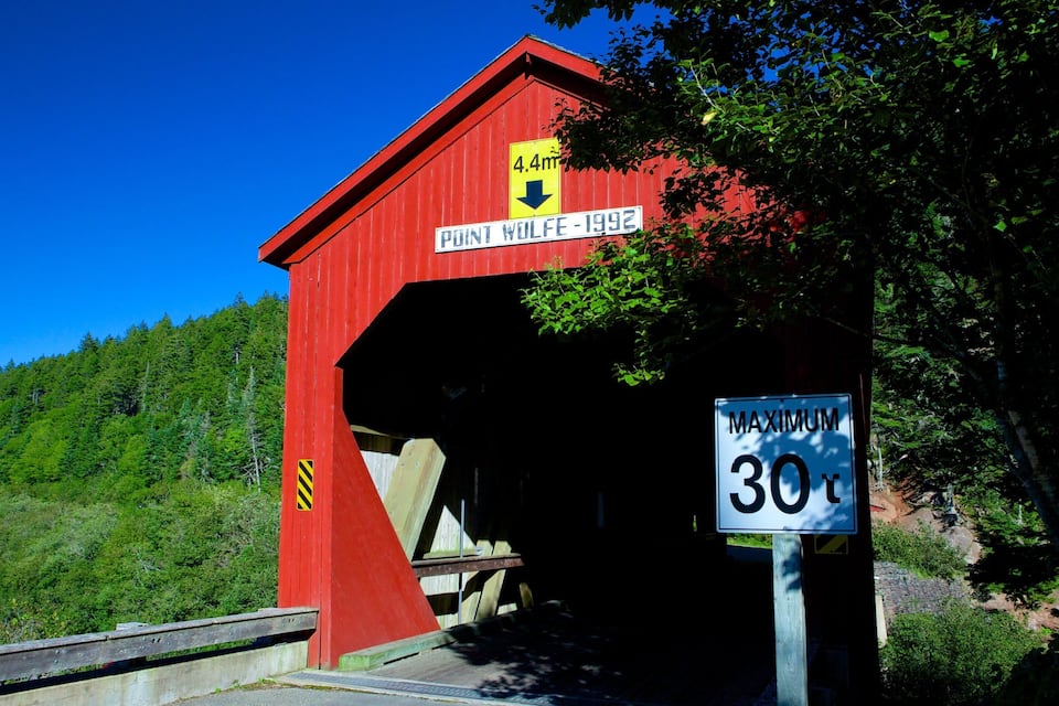 Eine rote gedeckte Brücke mit einem Schild, das eine Höchstgrenze von 4,4 Metern und eine Höchstgeschwindigkeit von 30 km/h anzeigt.