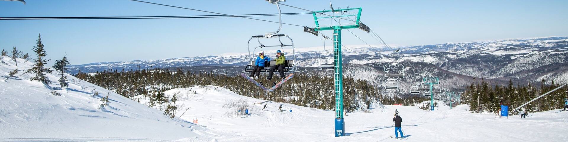 A ski lift with skiers and a snowy mountain landscape.