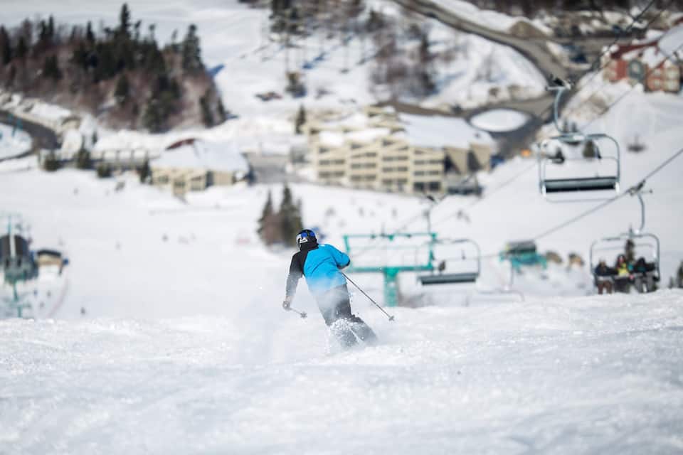 A skier descending a snowy slope with a ski lift in the background.