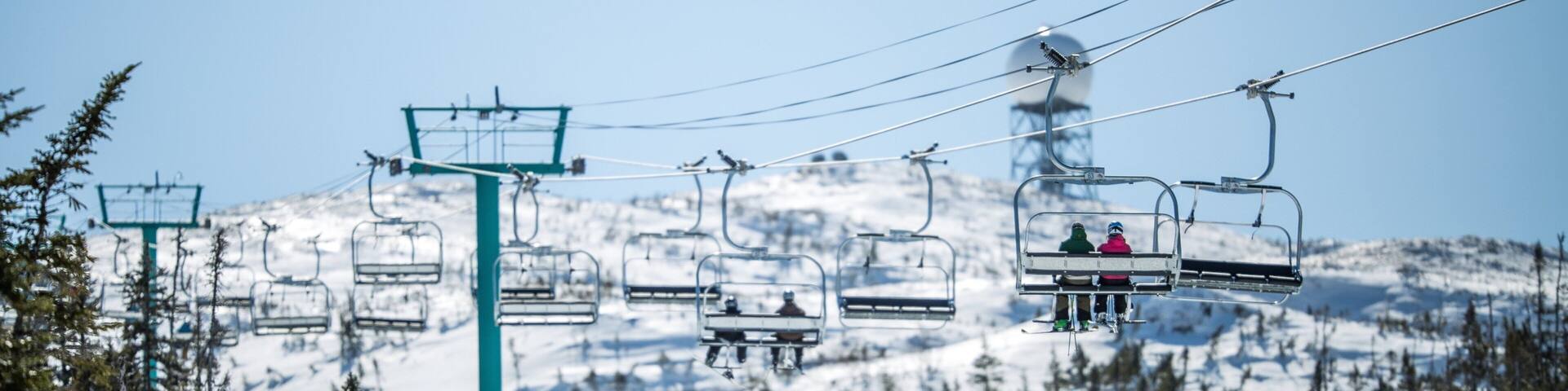 A ski lift with skiers and snowboarders on a snowy mountain slope.