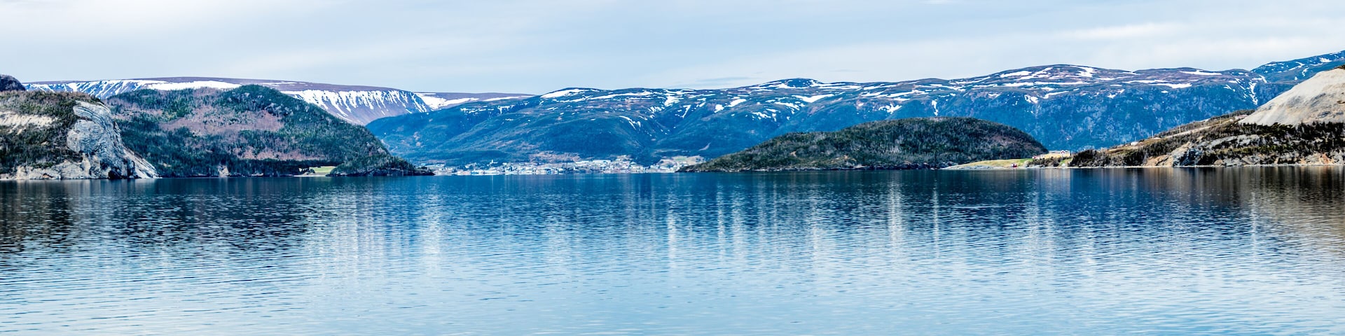 Ein ruhiger See, umgeben von schneebedeckten Bergen und dichten Wäldern.