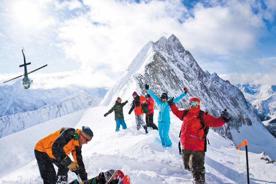 A group of people on a snowy mountain with a helicopter in the background.