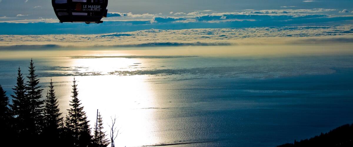 A cable car over a body of water with a reflection of the sun.