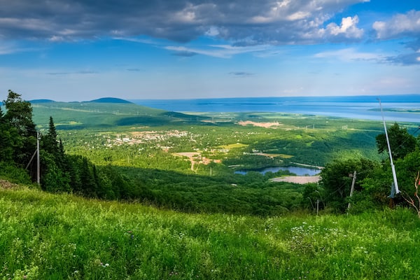 Un paysage verdoyant et luxuriant, avec un lac, une petite ville et des montagnes lointaines, le tout sous un ciel partiellement nuageux.