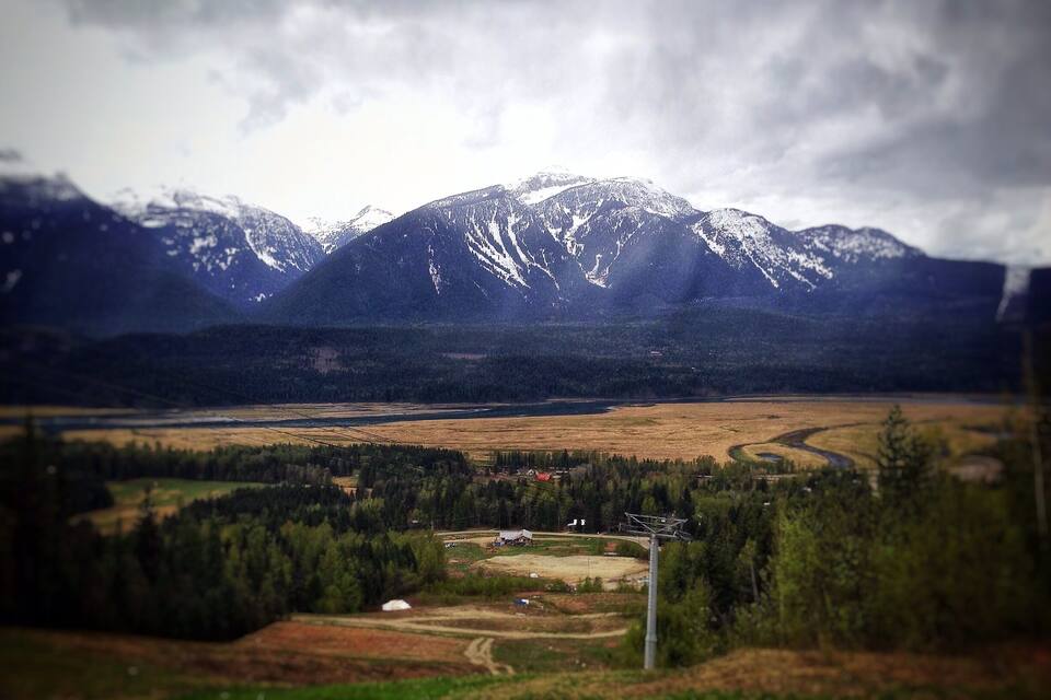 A mountainous landscape with snow-capped peaks, a valley with fields, and a small settlement.