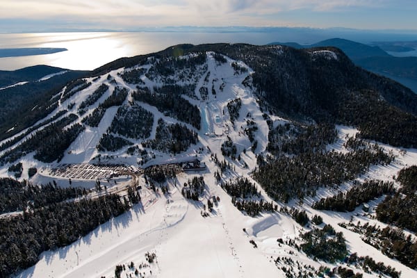 A snow-covered mountain with ski trails and a parking area.