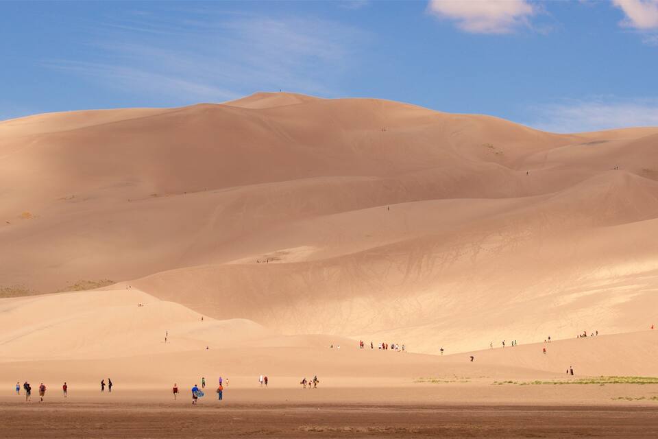 A desert landscape with rolling sand dunes and a clear blue sky.