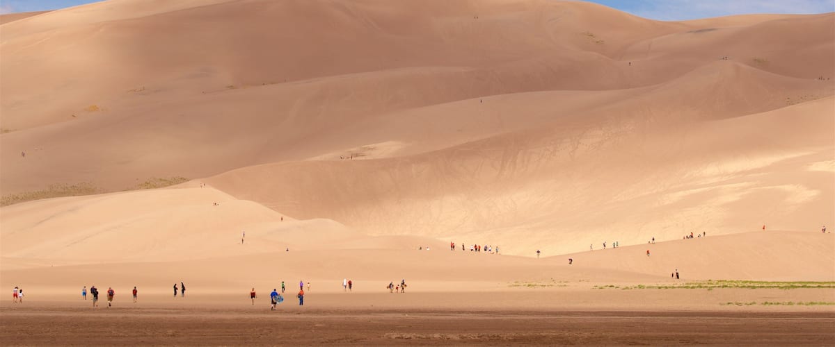 A desert landscape with rolling sand dunes and a clear blue sky.