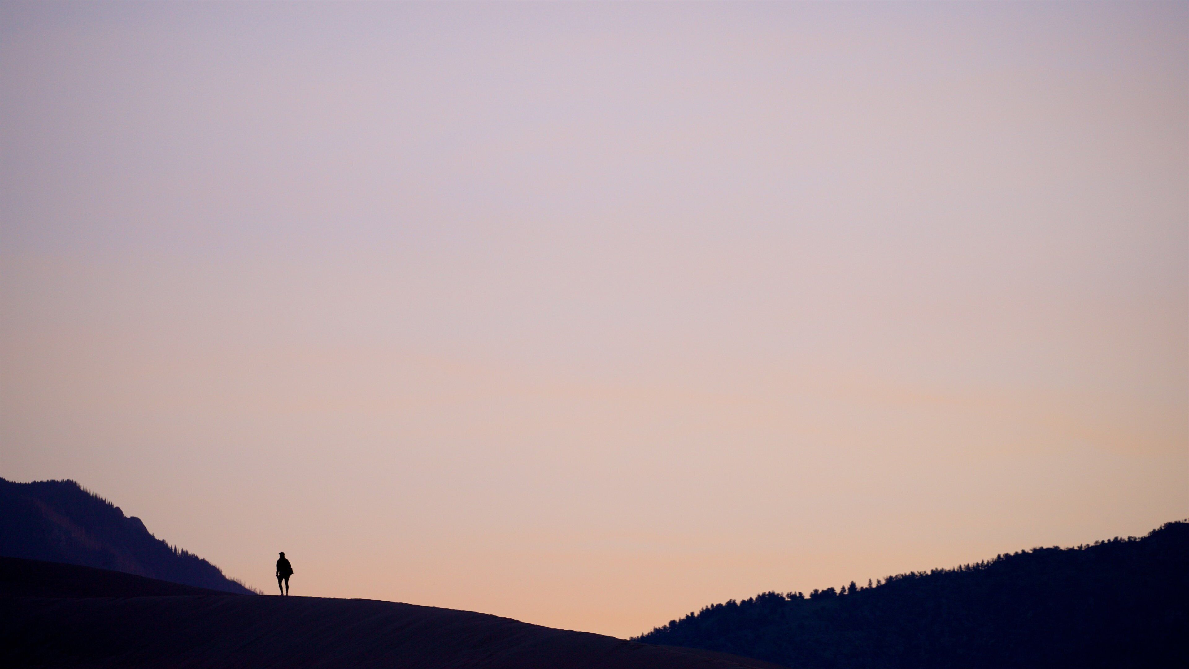 A silhouette of a person standing on a hill with a clear sky.