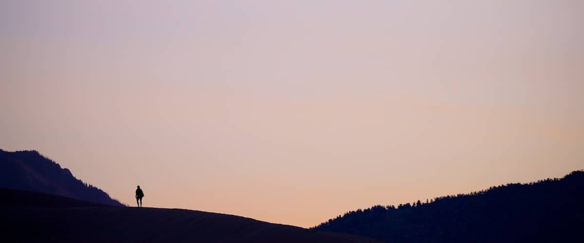 A silhouette of a person standing on a hill with a clear sky.