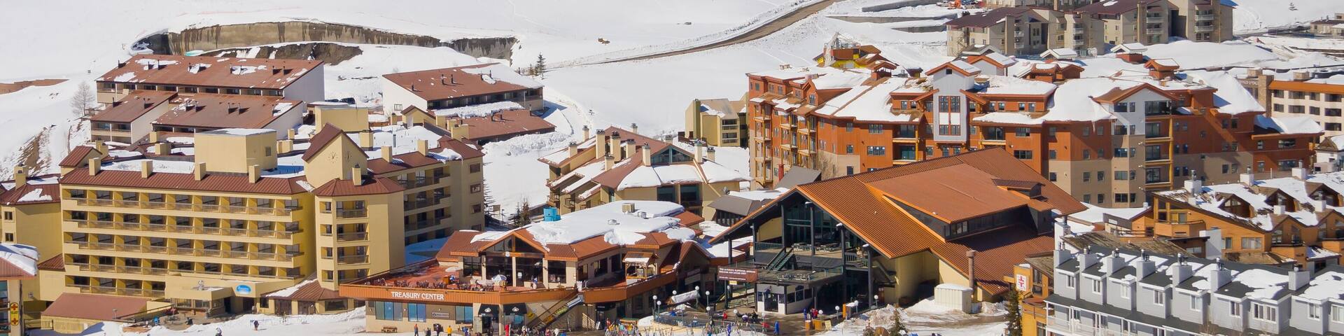A snow-covered ski resort with buildings, ski slopes, and mountains in the background.