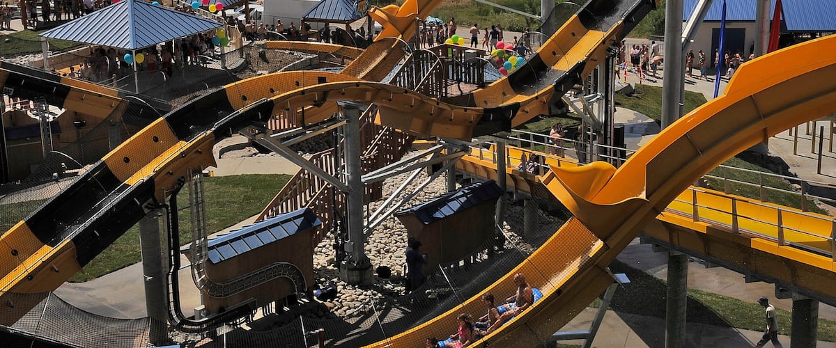 A roller coaster with multiple tracks and cars, surrounded by a park area with tents and people.
