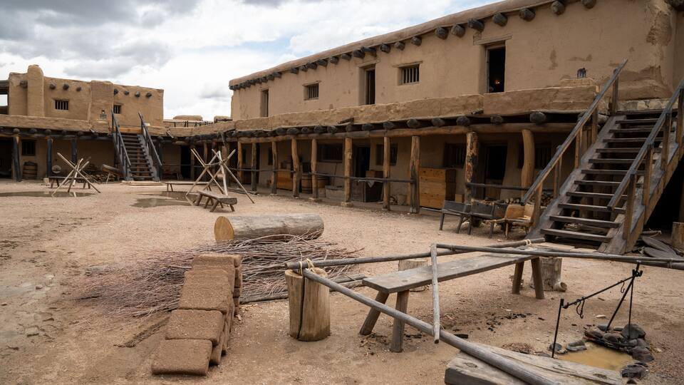 A traditional adobe building with wooden staircases and a dirt courtyard.