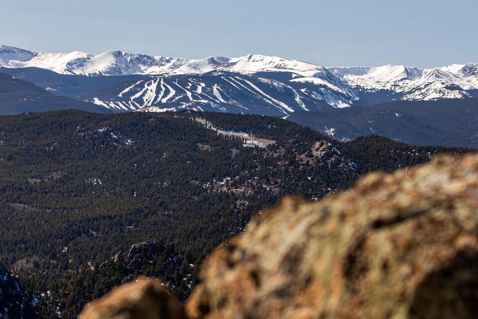 Paisagem montanhosa com picos nevados e florestas densas.