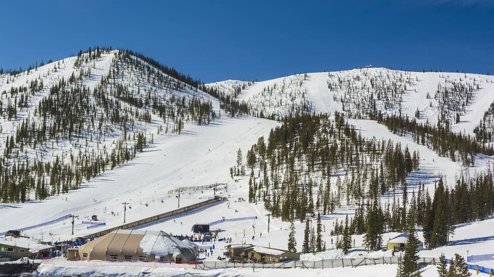 A snow-covered ski slope with a ski lift, a parking lot, and a lodge.