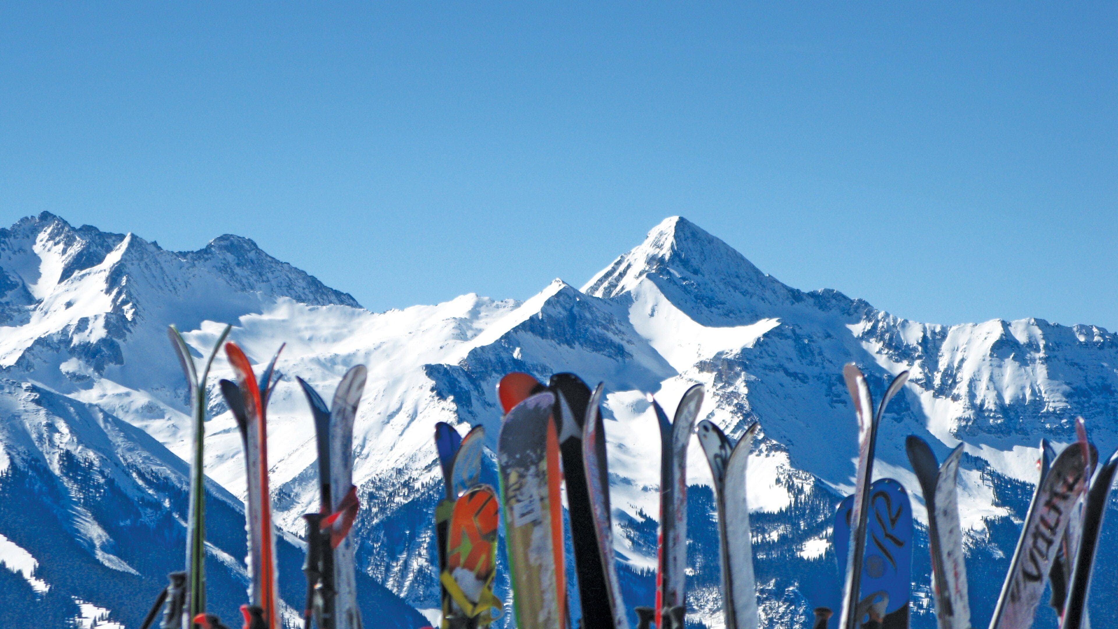 Una hilera de esquíes en primer plano con montañas nevadas al fondo.